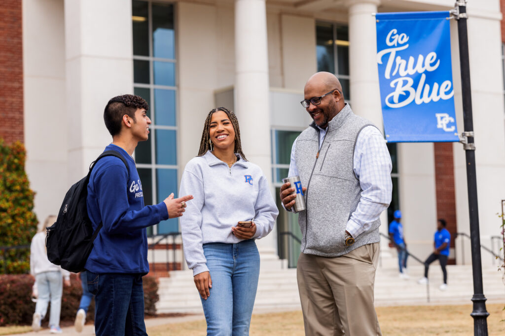Two students and a professor speaking on campus.