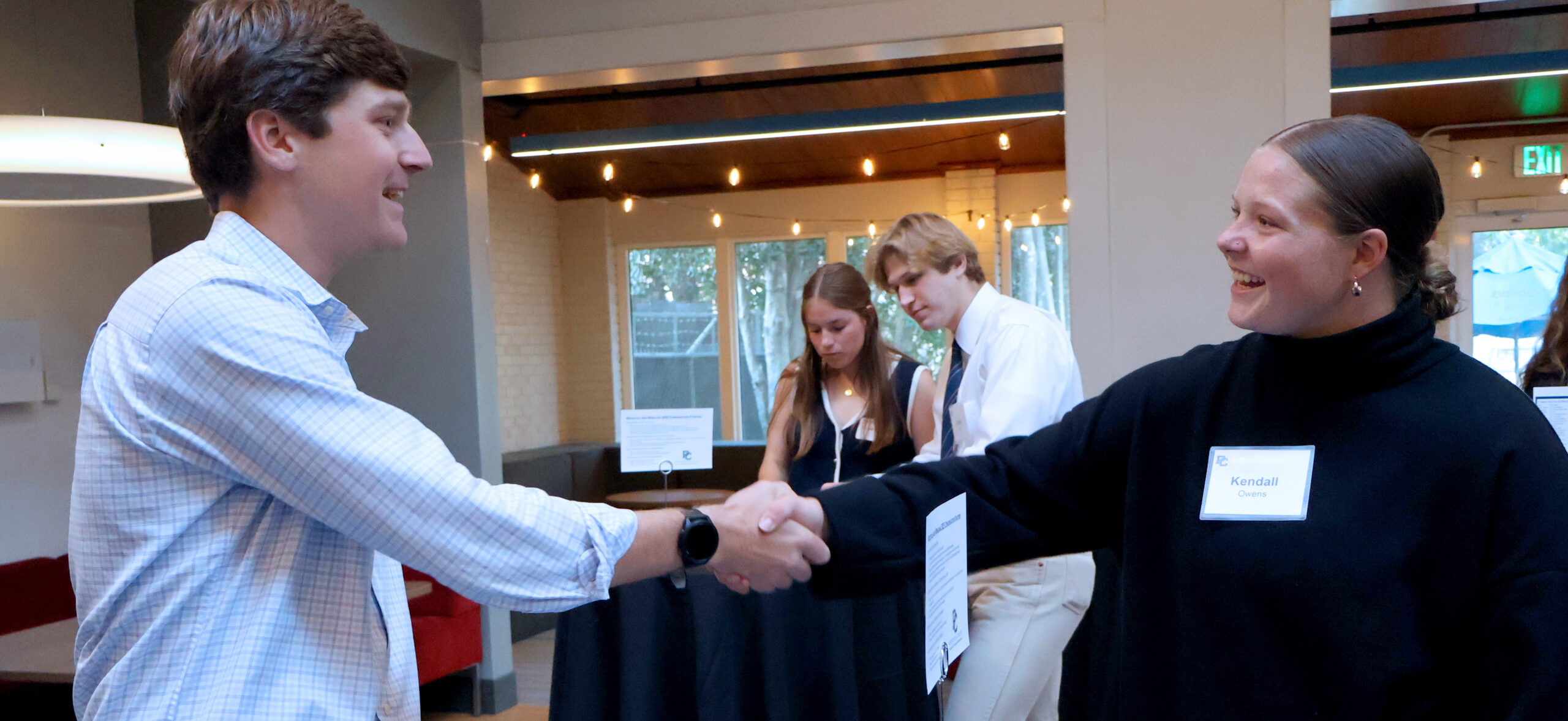 PC alum and current student shake hands at a networking event.